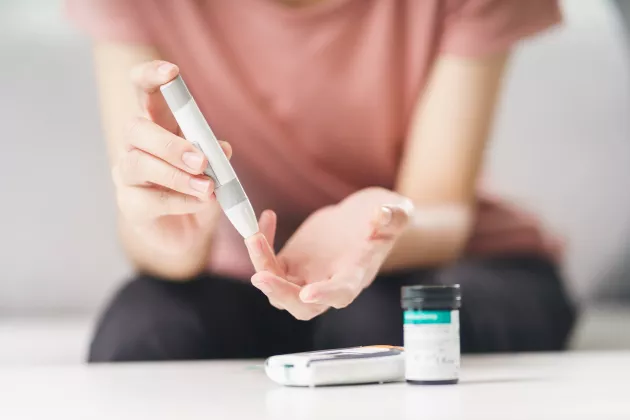 Woman using lancet on finger for checking blood sugar level. Photograph.